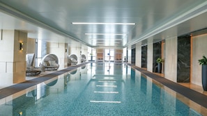 Une longue piscine intérieure à l’eau claire, entourée de murs au design moderne et dotée d’espaces où l’on peut s’asseoir le long des côtés.