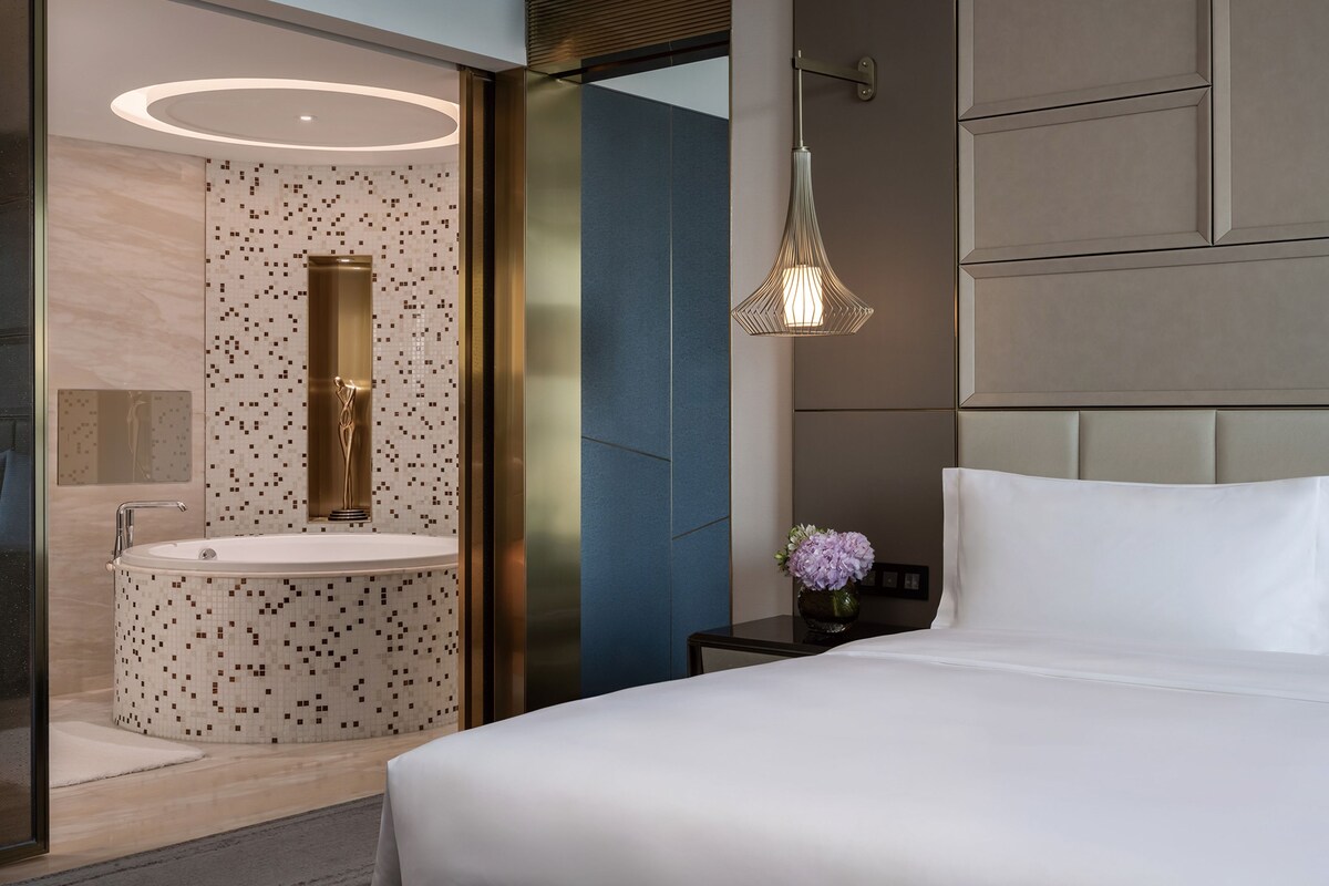 A modern hotel room with a large bed, a round sink, and a decorative light fixture.