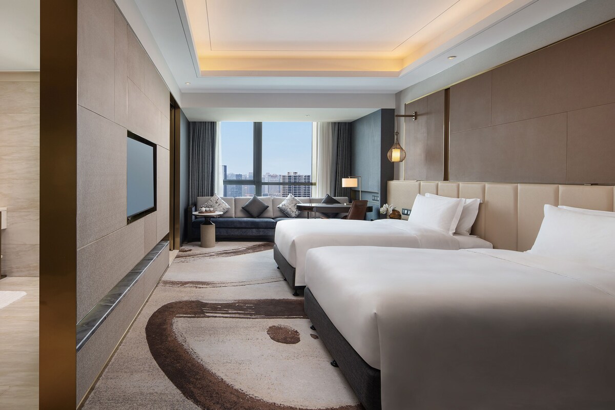 A hotel room with a large bed, a sofa, a desk, and a view of the city.