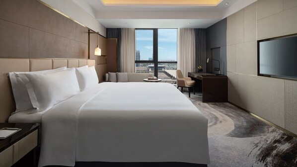 Une chambre d’hôtel avec un grand lit, un bureau, une chaise, une télévision et une vue sur le paysage urbain.