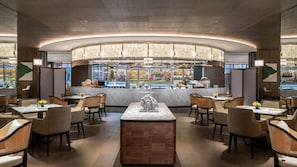 Um restaurante moderno com um bar central, assentos ao redor e vista para a cozinha.