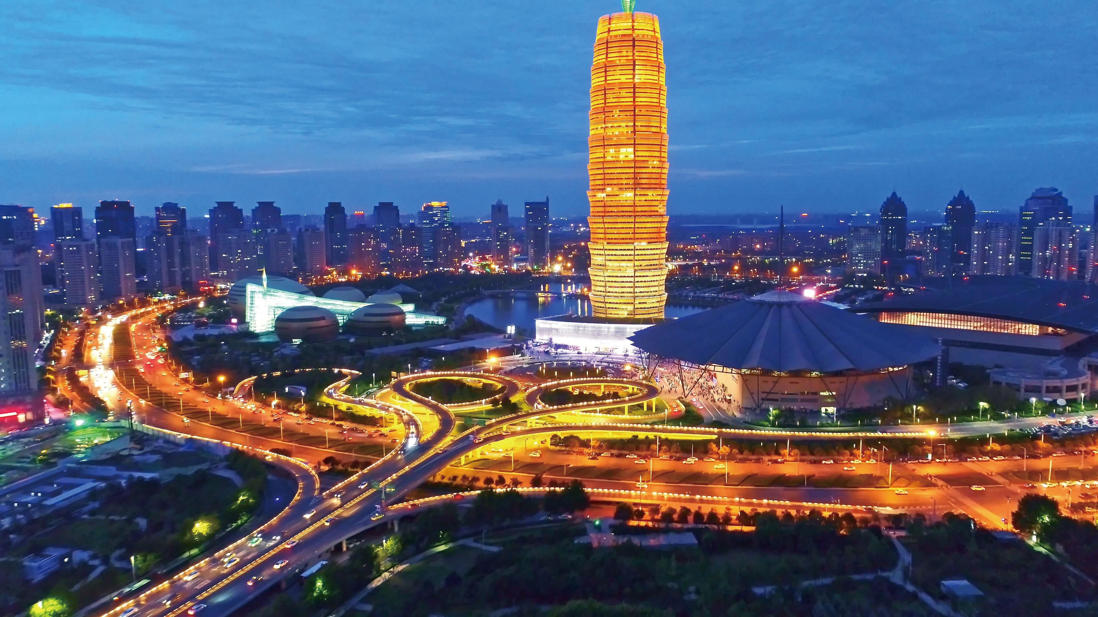 A cityscape with a prominent, illuminated tower, a roundabout with multiple exits, and surrounding high-rise buildings.