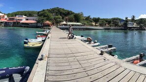 A wooden pier with boats docked on both sides, leading to a waterfront area with buildings and greenery in the background. - Villa with sea view in the heart of Sainte-Anne (Martinique)