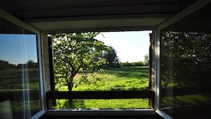 Ein Zimmer mit großem Fenster und Blick auf eine Wiese mit Bäumen.