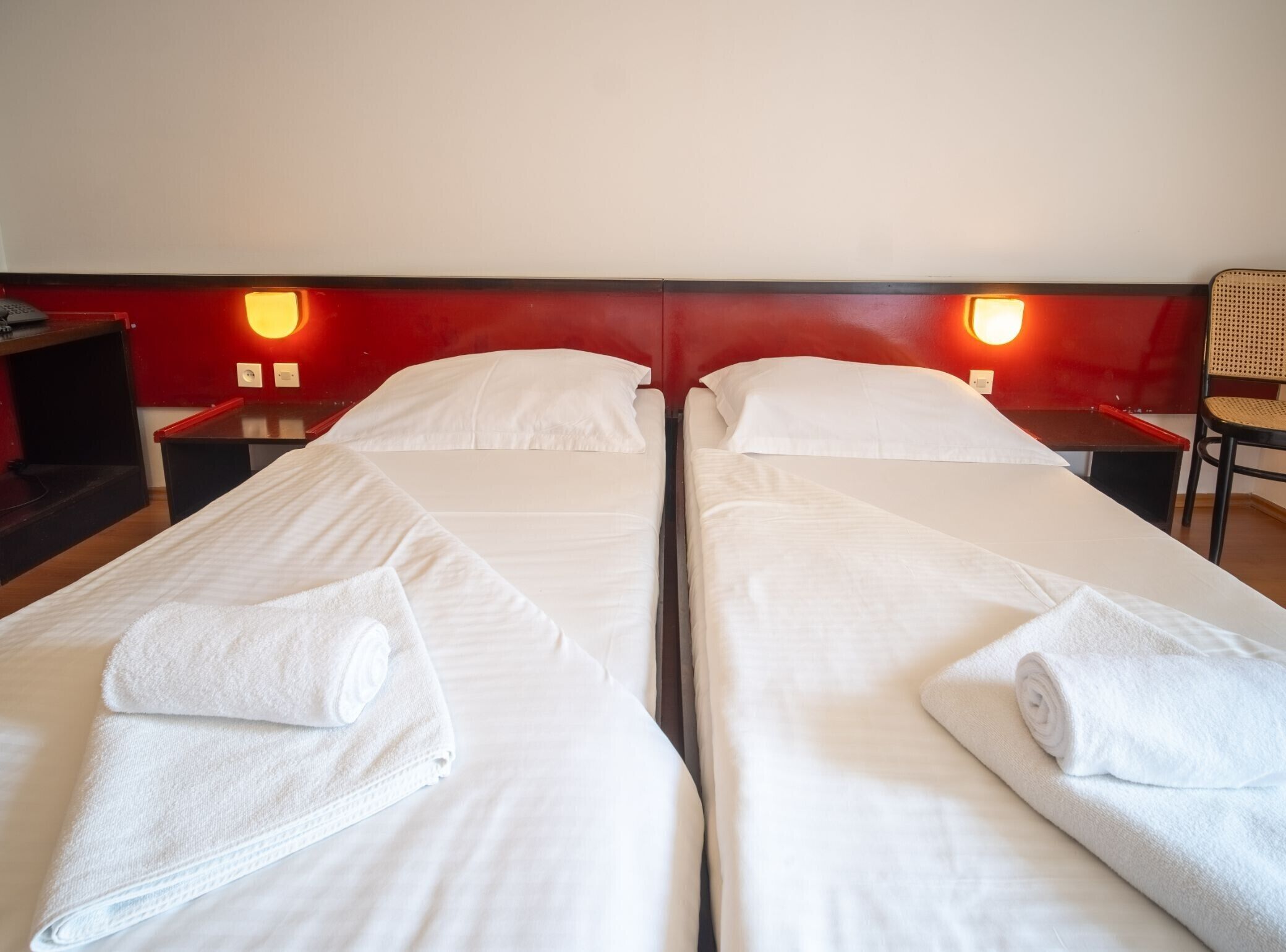 A hotel room with two single beds, each with a neatly folded white towel.