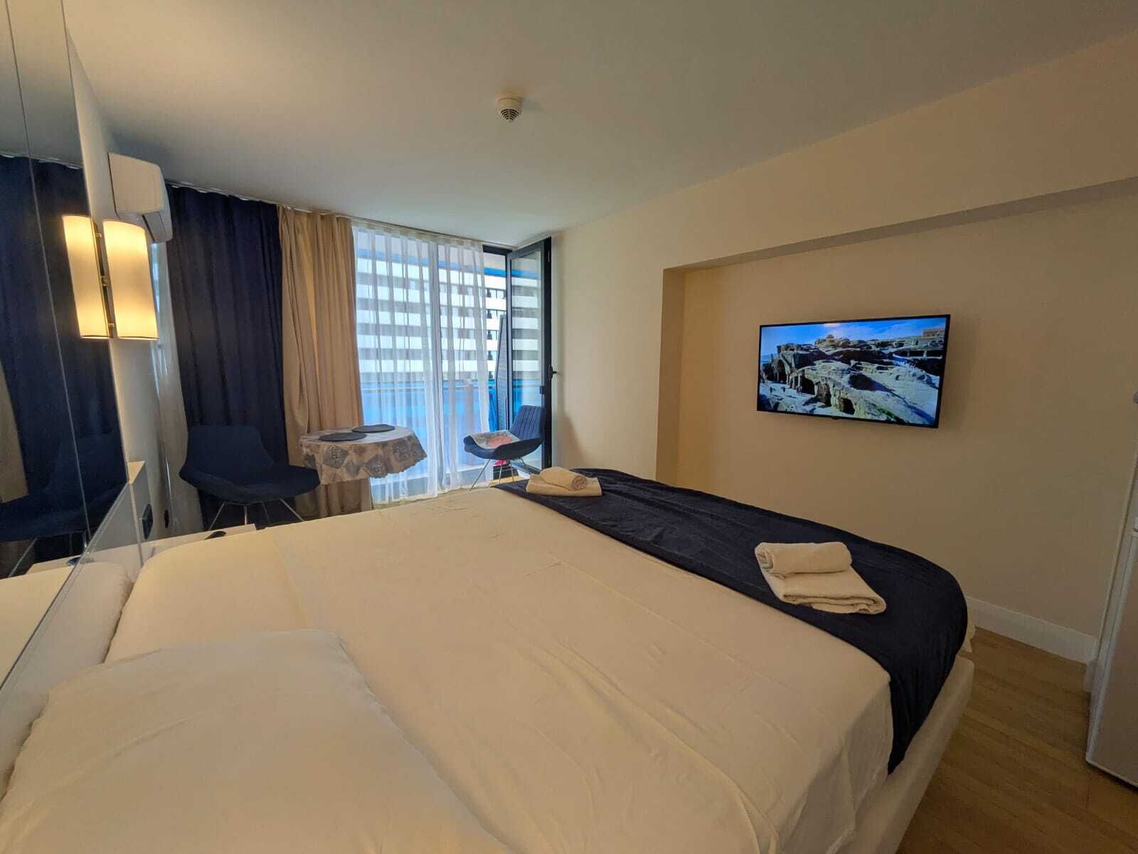 Een hotelkamer met een bed, een bureau, een stoel, een televisie en een balkon met gordijnen.