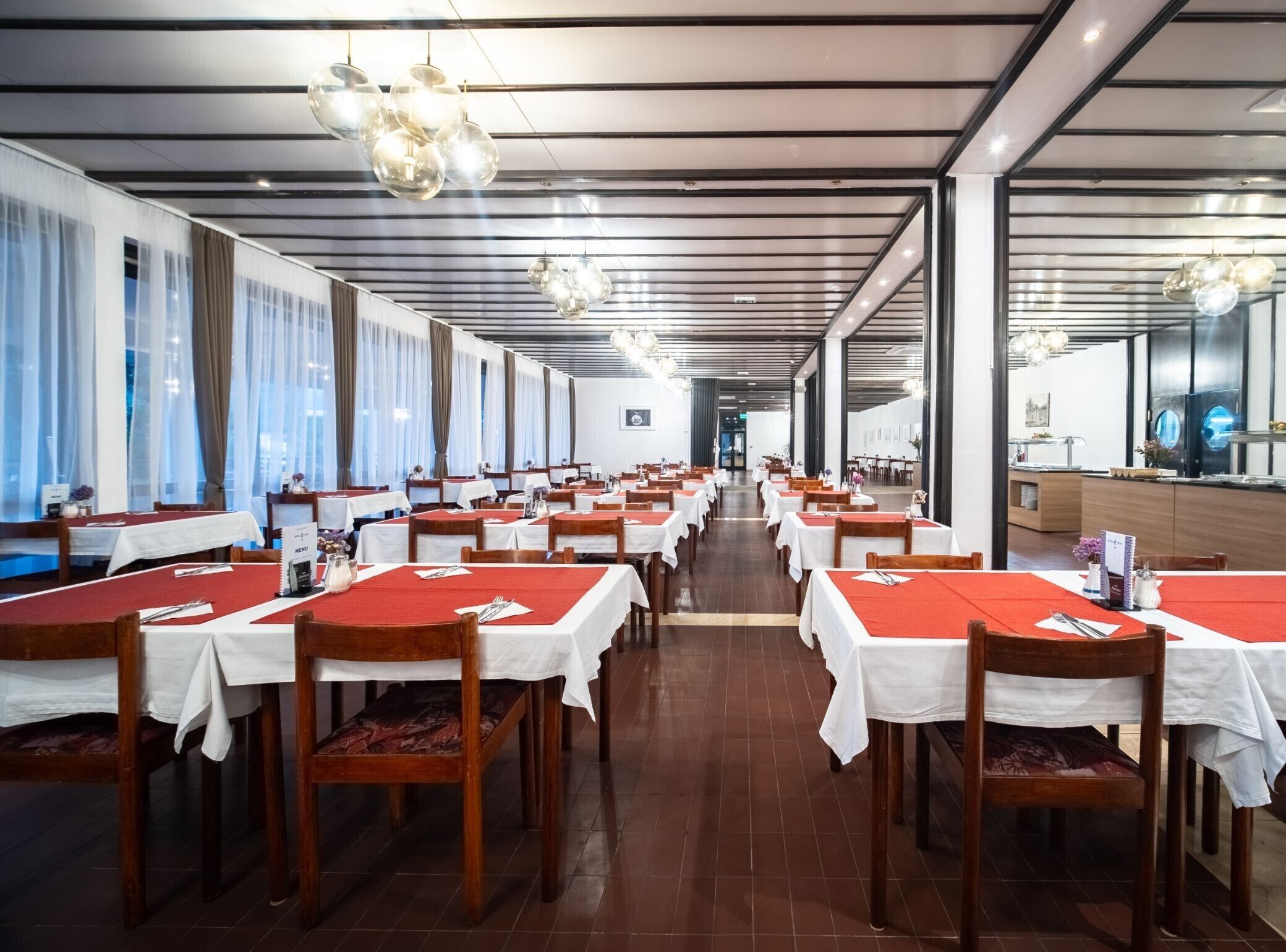 A spacious dining area with long tables, wooden chairs, and modern pendant lighting.