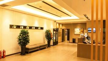 Un vestíbulo de hotel con mostrador de recepción, zona de estar y plantas en macetas.
