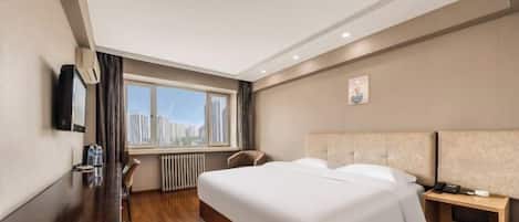 A hotel room with a bed, a desk, a chair, a nightstand, and a window with a city view.