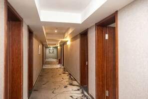 A hotel corridor with wooden doors, a patterned carpet, and a ceiling light fixture.