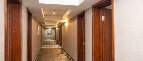 A hotel corridor with wooden doors, a patterned carpet, and a skylight ceiling.