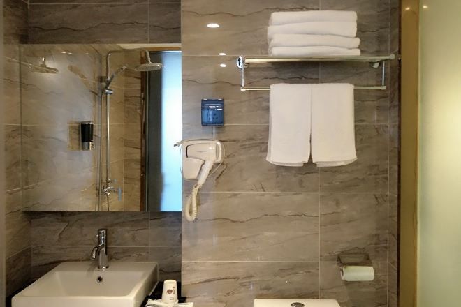 Un baño con lavamanos, espejo, ducha y toallero.