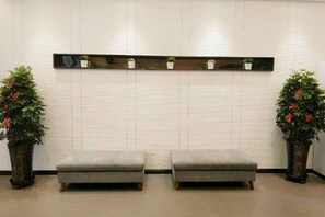 A reception area with two grey cushioned seating, a wall-mounted shelf with potted plants, and a tiled wall. - Homeinn Ripple Hotel (Harbin Xuefu Road Kaide Plaza) (Harbin)