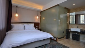 Hotellihuone, jossa on sänky, lasiseinäinen suihkukaappi, pesuallas ja suuri ikkuna.