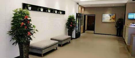 A hotel reception area with a reception desk, seating area, and potted plants.