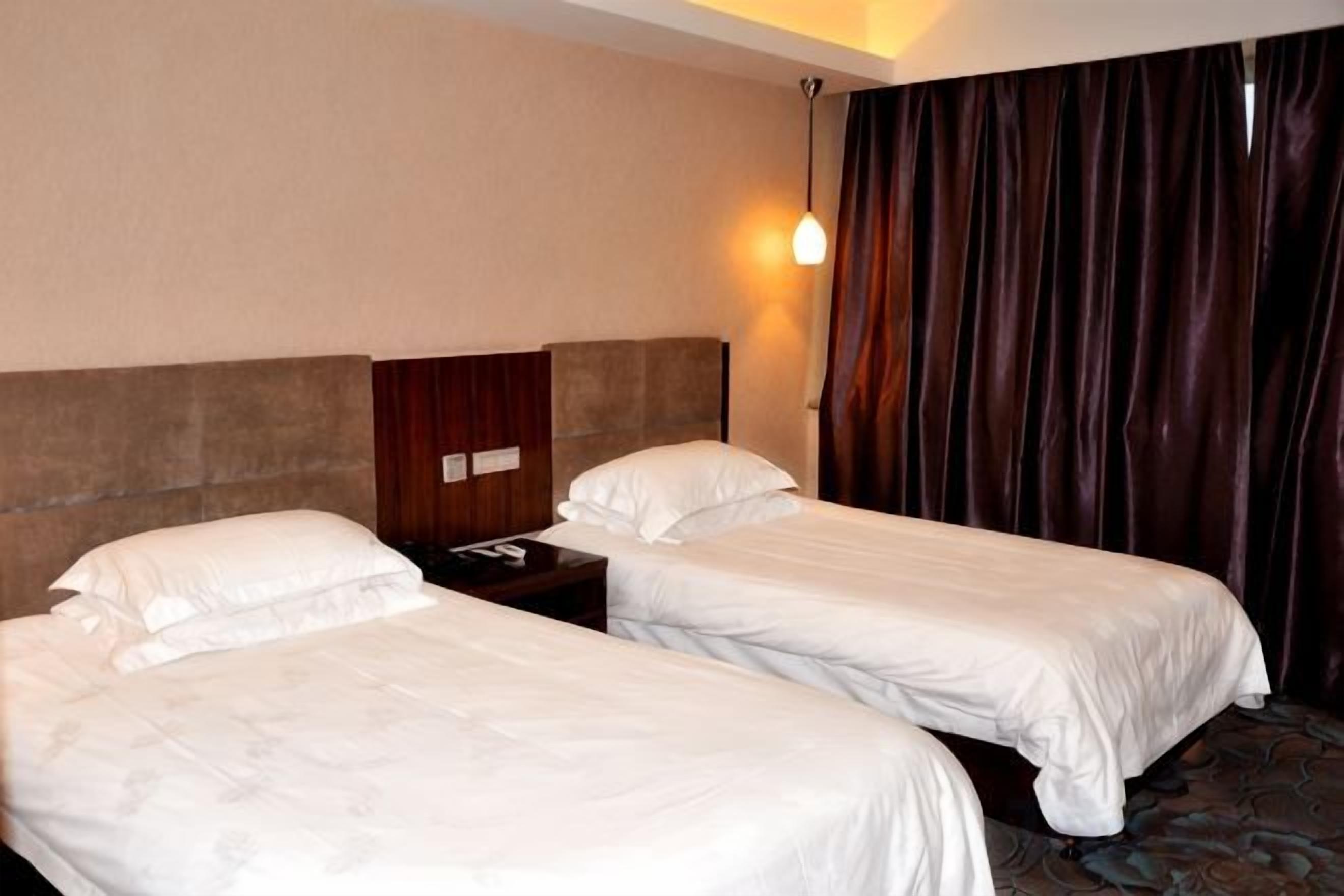 Una habitación de hotel con dos camas individuales, una mesita de noche, una lámpara y una cortina.