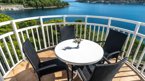 Un balcon avec une table ronde et quatre chaises, donnant sur une étendue d’eau et une zone verdoyante.