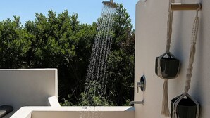 A modern outdoor shower area with a wooden floor, a wall-mounted faucet, and a hanging macrame container.