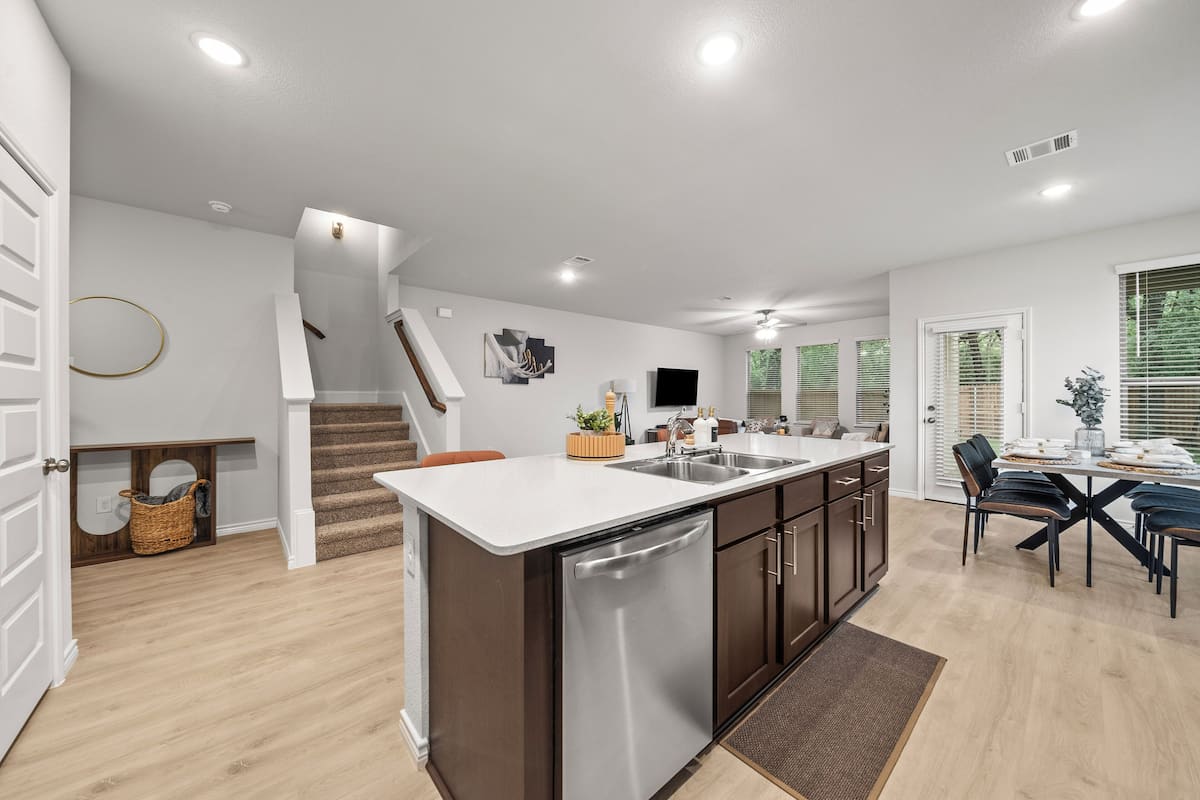 A modern kitchen with a dishwasher, a dining area with a table and chairs, and a staircase leading to another level.