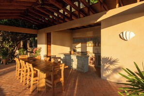 Un área de cocina al aire libre con mesa y sillas, una barra integrada y un muro de piedra decorado con conchas.