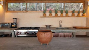 A kitchen with a stove, sink, and a window with a shelf holding pineapples. - Monte LaLaLa - Eco-Lodge à Mermejita - Vue imprenable depuis la piscine! (Oax.)