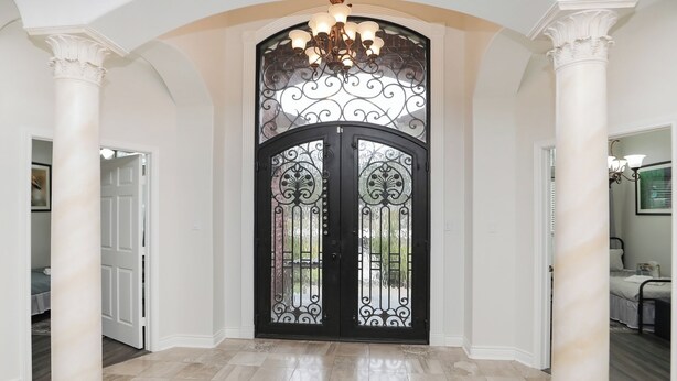 A grand entrance with a black ornate door, white columns, and a chandelier.