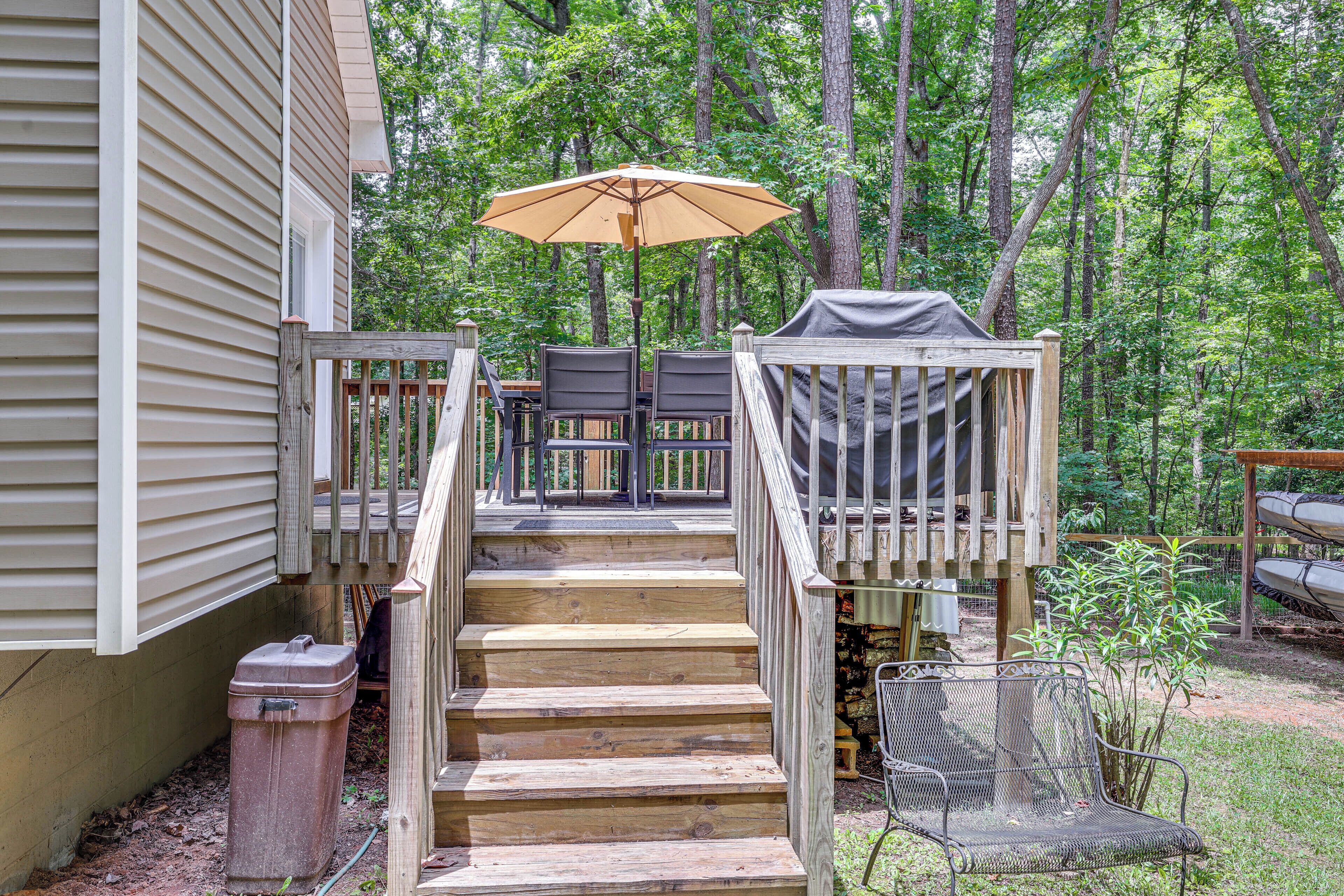 A wooden deck with a set of stairs leading to a covered seating area, surrounded by trees.