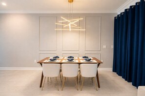 A dining area with a table set for four, a modern pendant light, and a blue curtain.