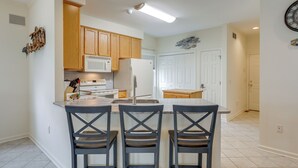 A kitchen with wooden cabinets, a white refrigerator, a microwave, and a sink. There are three bar stools and a countertop. - Waterfront Gem w/ Dock: 3 Mi to Fenwick Island Fun (Selbyville)