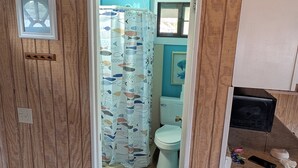 Ein kleines Badezimmer mit Toilette, einer Duschkabine mit Fischmuster und Holzboden.
