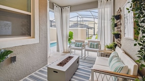 Un espace de vie extérieur moderne, avec un canapé blanc, un foyer et des plantes en pot.