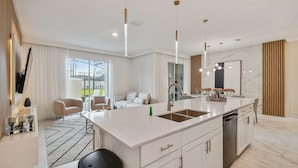 Une cuisine moderne dotée d’un grand îlot central, de meubles blancs et d’un éclairage suspendu.