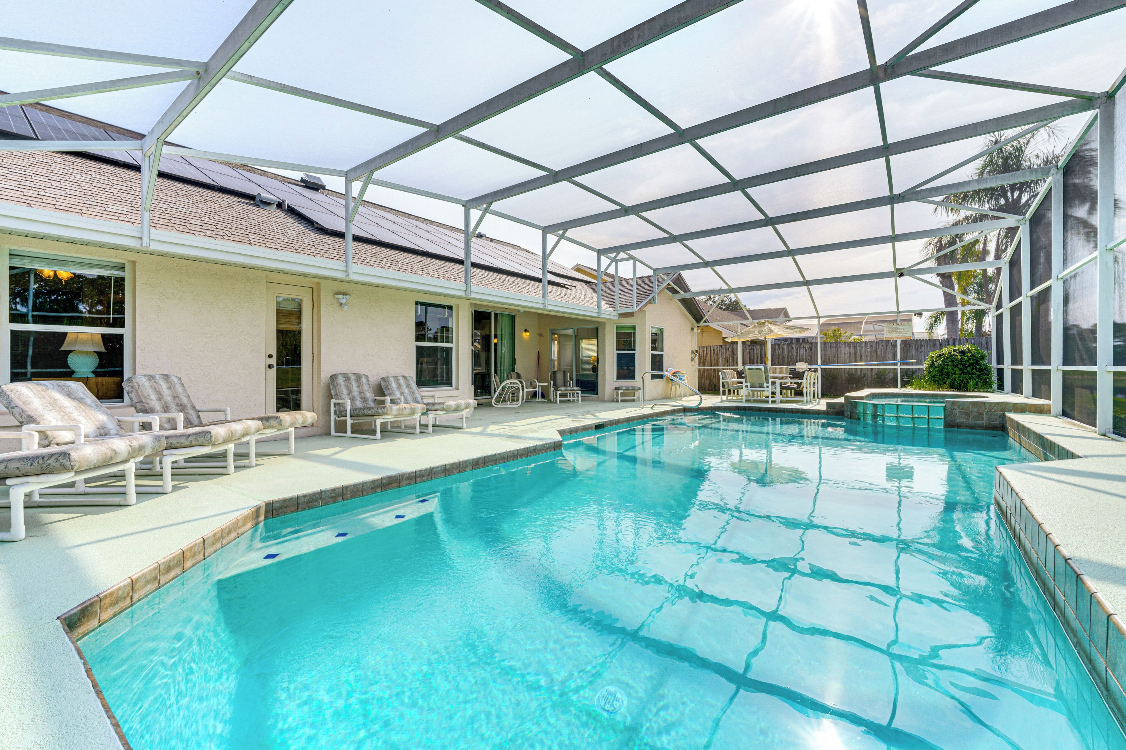 Une piscine entourée de parois en verre, des chaises longues et un espace patio couvert.