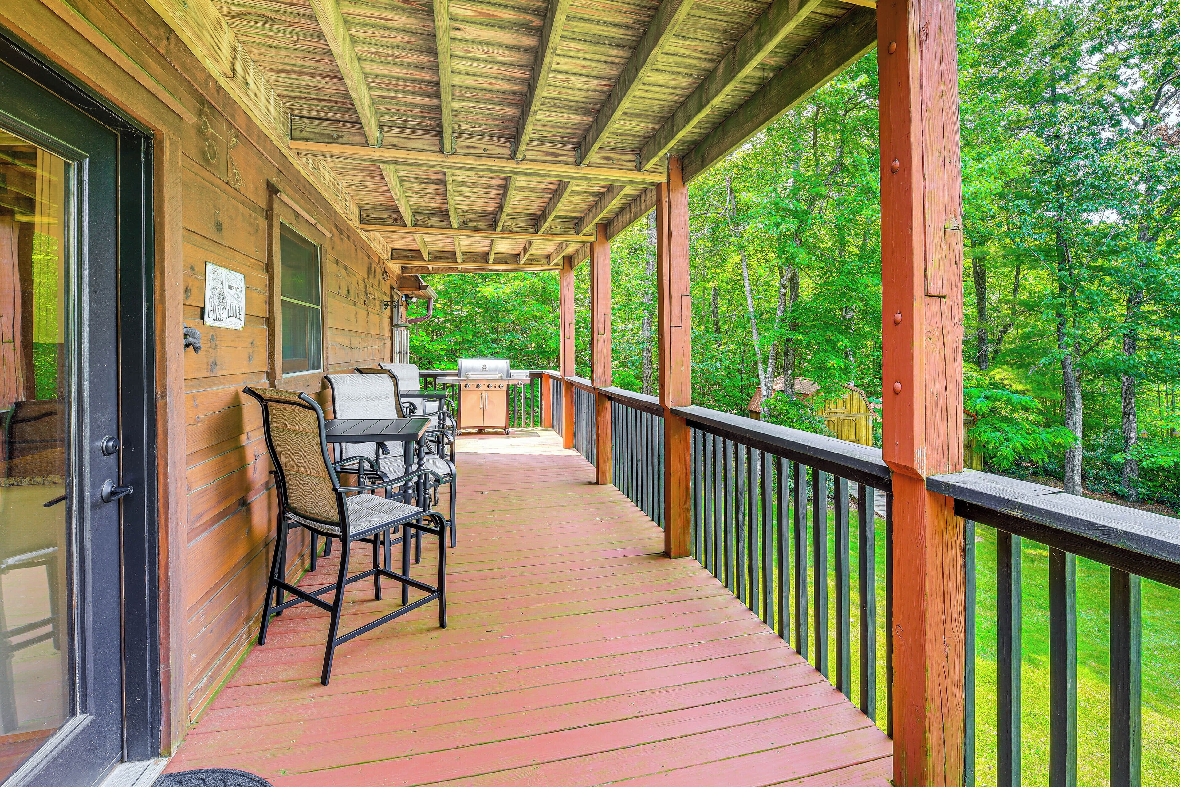 A wooden deck with a covered area, outdoor seating, and a view of a forested area.