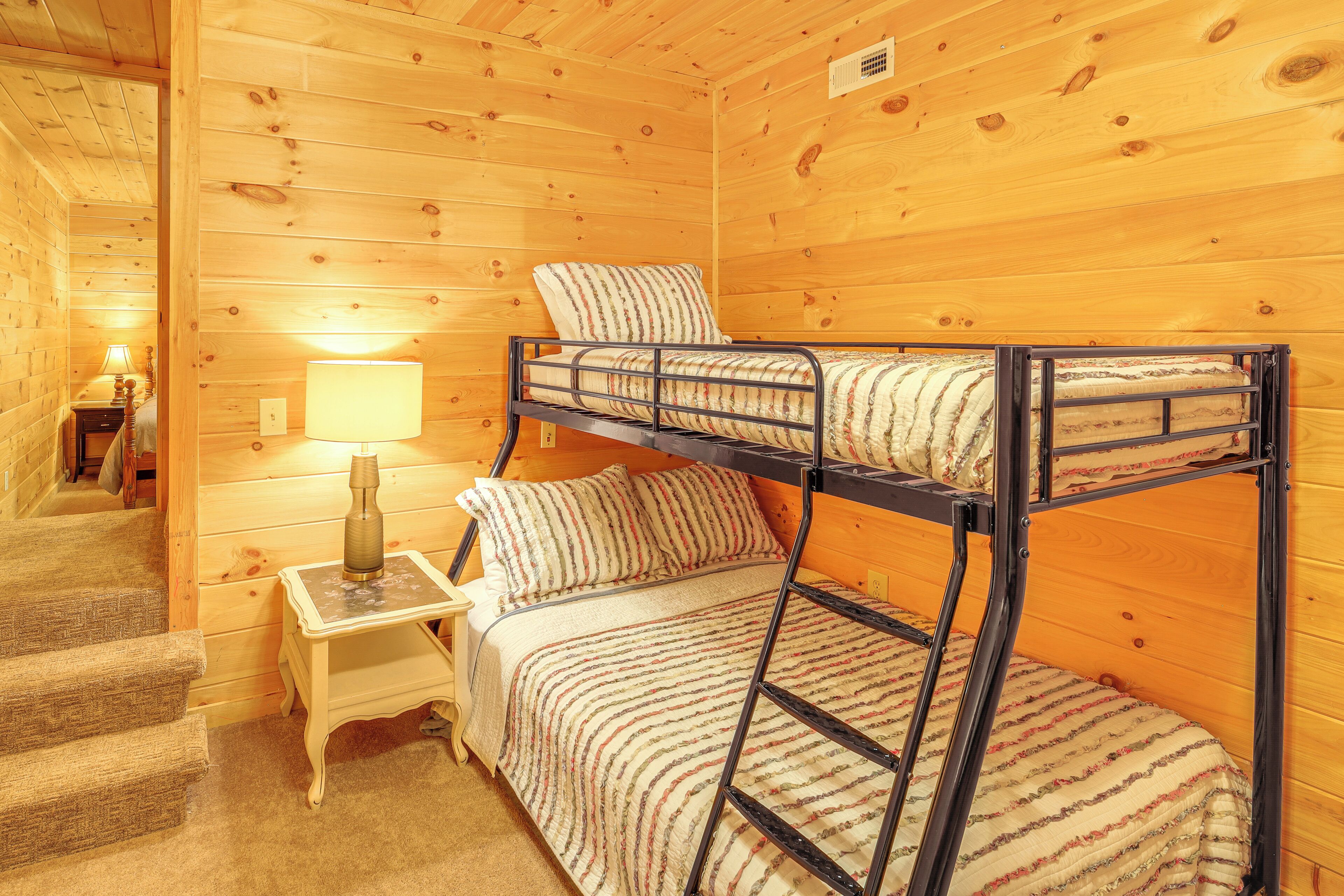 Een slaapkamer met stapelbedden, houten inrichting, een nachtkastje met lamp en een trap naar een andere kamer.