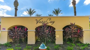 De ingang van Vista Cay Resort, met een gele gevel, boogvormige deuropeningen en tropische planten.