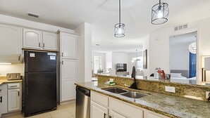 Een moderne keuken met witte kastjes, een zwarte koelkast, een roestvrijstalen spoelbak en granieten aanrechtbladen.