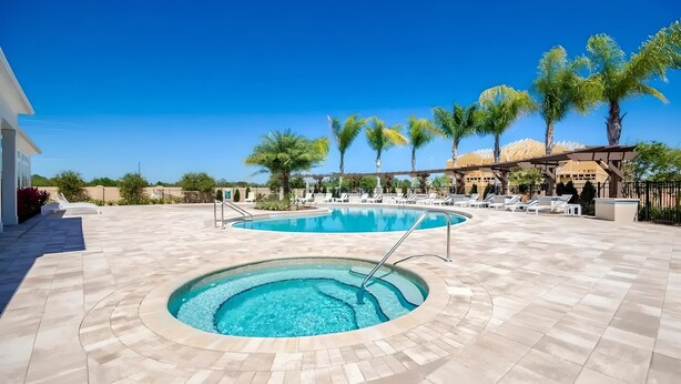 A pool area with a hot tub, lounge chairs, and palm trees. - 3BR Home with Resort Pool & Game Room (Kissimmee)