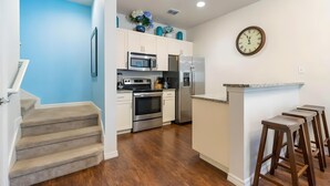 A modern kitchen with white cabinets, stainless steel appliances, and a wooden staircase. - 3BR Home with Resort Pool & Game Room (Kissimmee)
