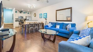 A modern living room with a blue sofa, a glass coffee table, and a dining area with a table and chairs. - 3BR Home with Resort Pool & Game Room (Kissimmee)