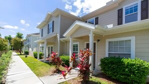 A row of townhouses with attached porches, a clear sky, and well-maintained lawns. - 3BR Home with Resort Pool & Game Room (Kissimmee)