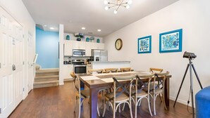 A modern kitchen with white cabinets, a dining table with six chairs, a clock, and two framed artworks on the wall. - 3BR Home with Resort Pool & Game Room (Kissimmee)