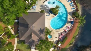 Luchtbeeld van een resort met een groot rond zwembad, een overdekt terras en een gebouw met een schuin dak.