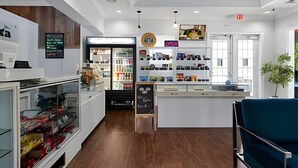 Een modern café interieur met een centrale toonbank, planken vol producten, een krijtbordmenu en een houten vloer.