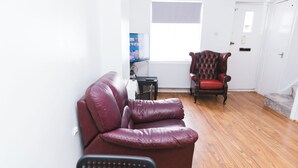 A living room with a leather sofa, a wooden floor, a red armchair, and a television on a stand.