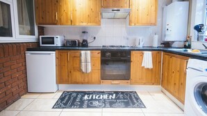 A kitchen with wooden cabinets, a microwave, a toaster, a blender, a kettle, and a washing machine.