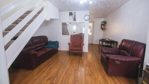 A living room with a wooden floor, a red leather sofa, a red armchair, and a staircase with white railings.