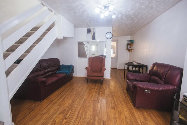 A living room with a wooden floor, a red leather sofa, a red armchair, and a staircase with white railings.