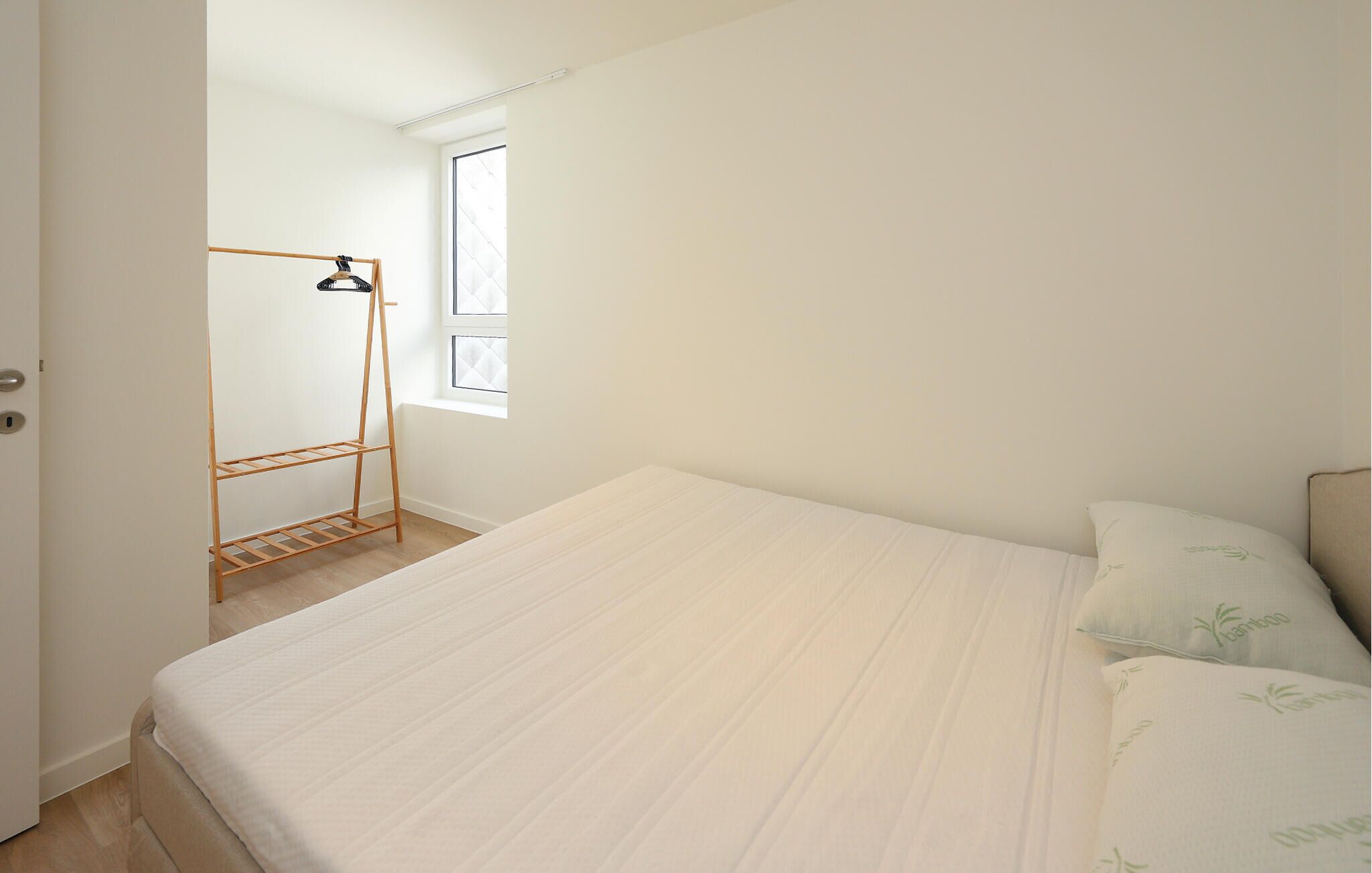 Ein Schlafzimmer mit einem Bett, einem Wäscheständer aus Holz und einem Fenster.