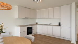 A modern kitchen with white cabinetry, a built-in oven, and a wooden dining table with chairs. - Lovely apartment in Oostende with WiFi (Oostende)